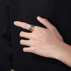 Hand wearing a silver ring against a black background