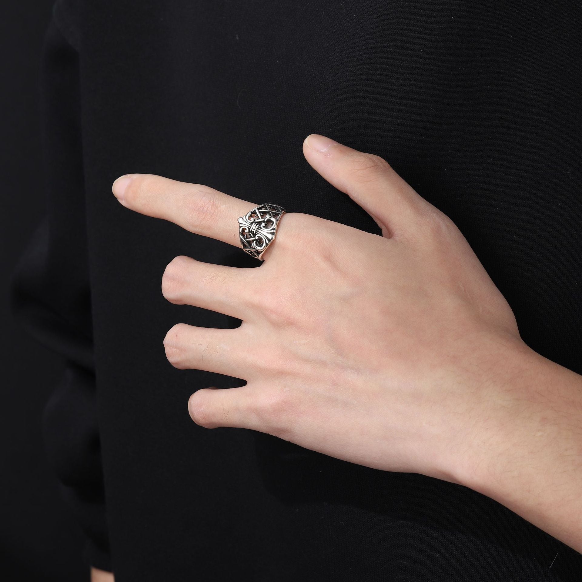 Hand wearing a silver ring against a black background