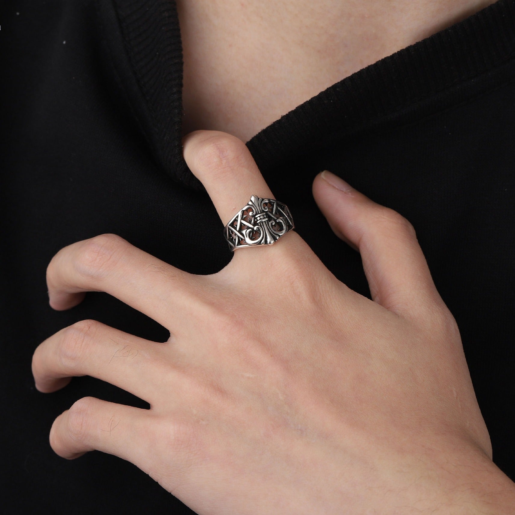 Hand wearing a silver ring with intricate design on a black background
