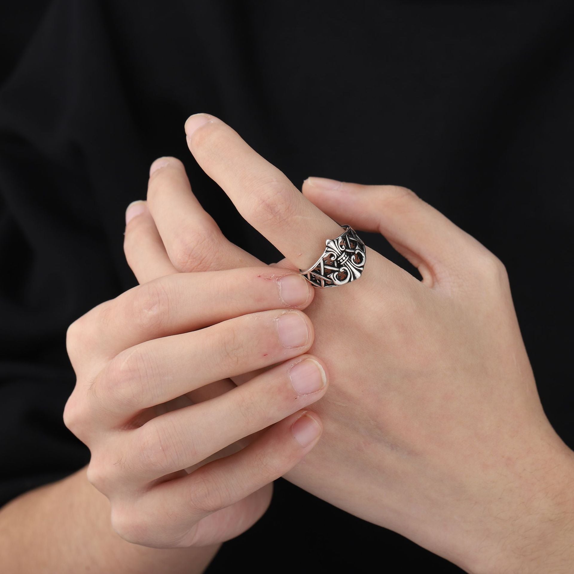 Close-up of a hand wearing a silver ring with intricate design on a black background
