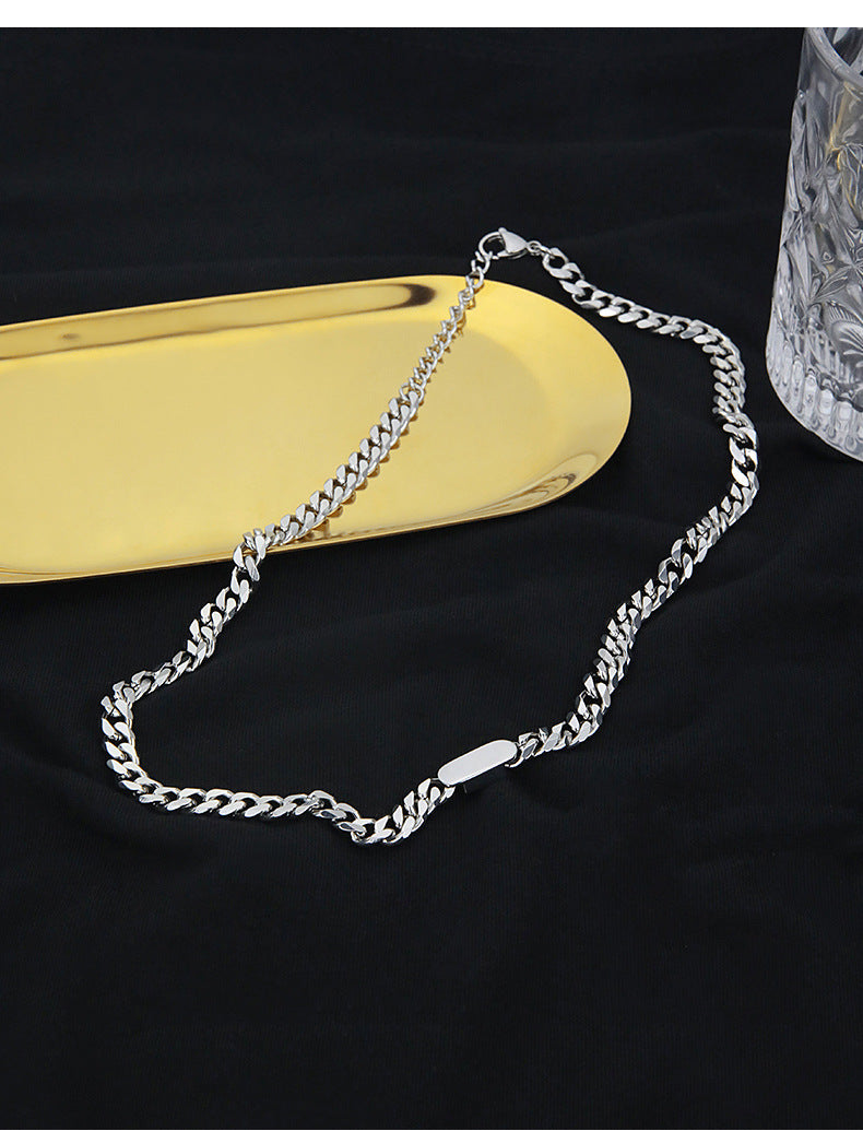 Silver chain necklace on a black background with a gold object and crystal vase.