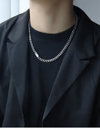 Person wearing a silver chain necklace with a plain background