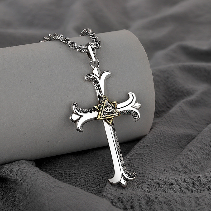 Silver cross necklace with a gold triangle pendant on a gray fabric background