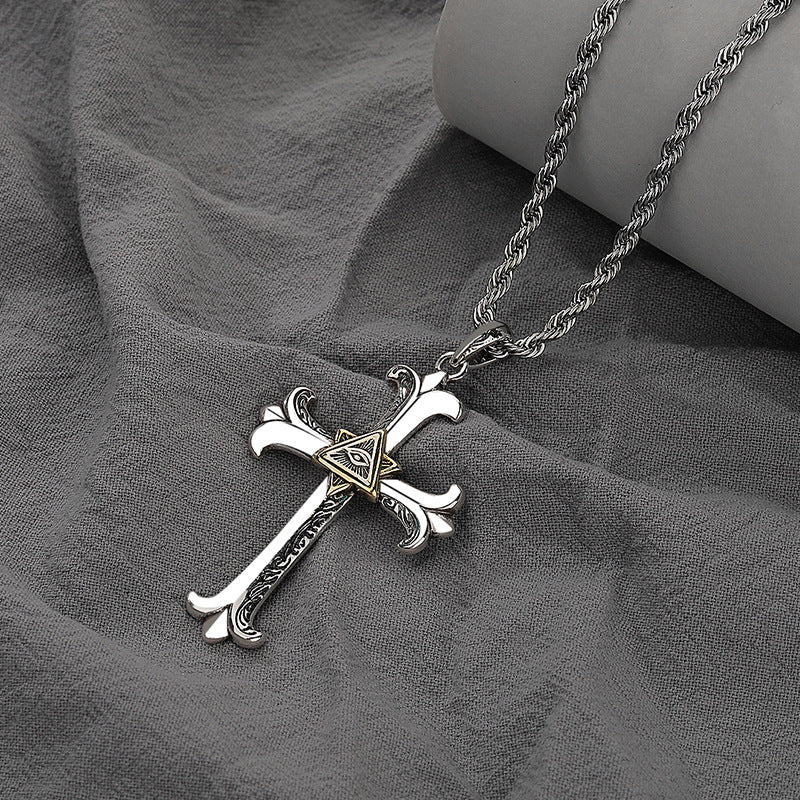 Silver cross necklace with a gold triangle pendant on a gray fabric background