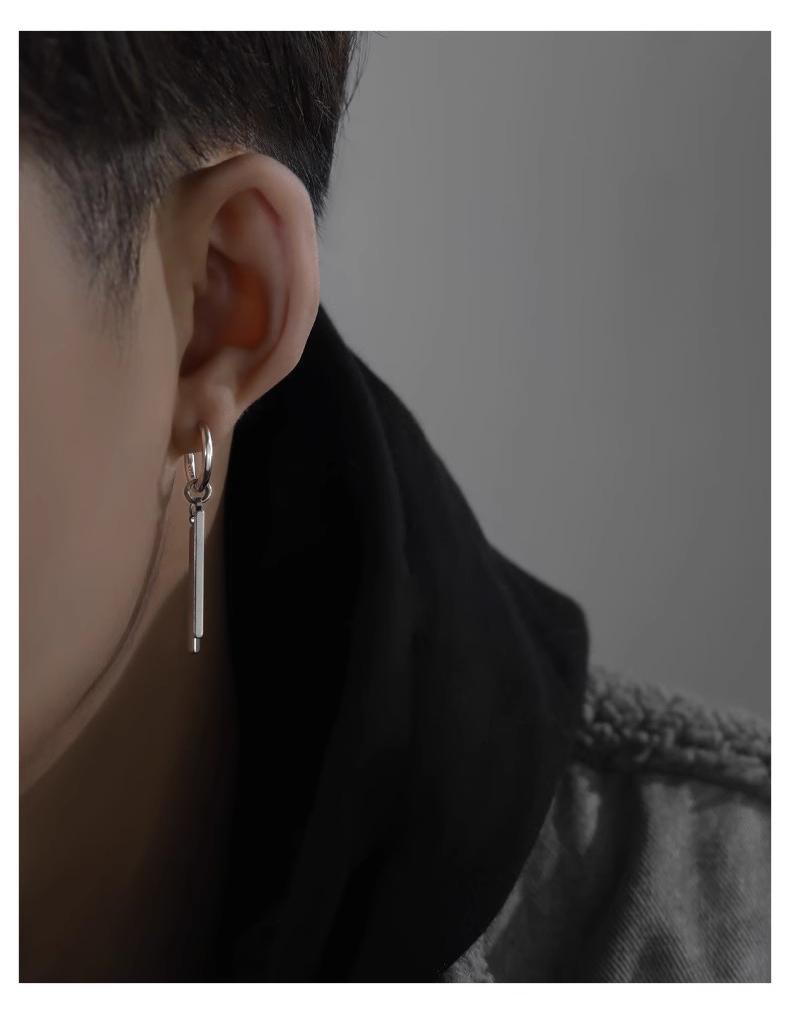 Close-up of an ear wearing a dangling earring with a neutral background