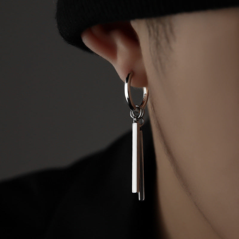 Close-up of a person wearing a silver hoop earring with a dangling bar on a dark background