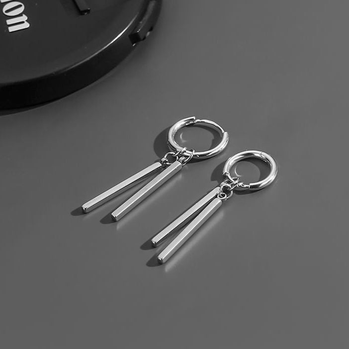 Silver hoop earrings with dangling bars on a dark surface
