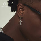 Close-up of an ear wearing a silver cross earring with a neutral background