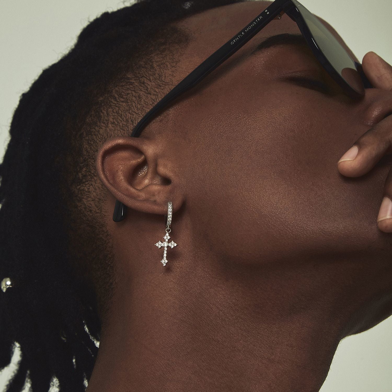 Close-up of an ear wearing a diamond cross earring with sunglasses on the head.