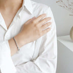 Person wearing a white shirt with a bracelet on a neutral background