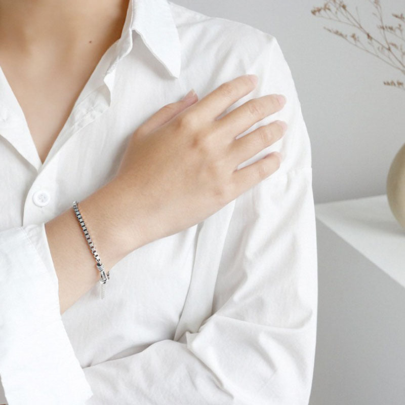 Person wearing a white shirt with a bracelet on a neutral background