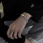 Close-up of a person's wrist with a silver bracelet and ring, sitting on a bench.