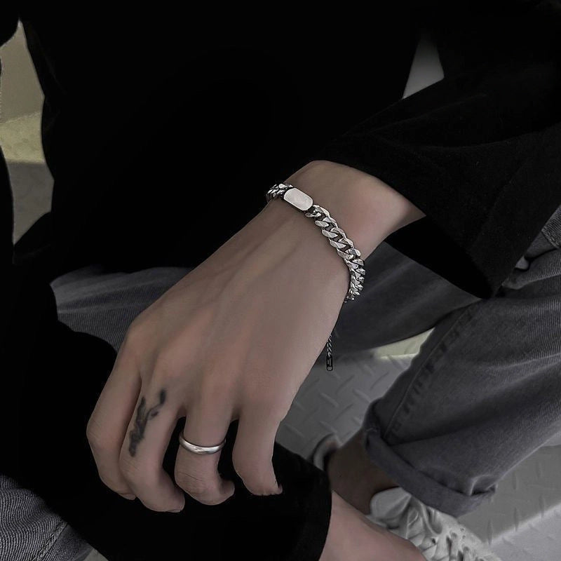 Close-up of a person's wrist with a silver bracelet and ring, sitting on a bench.