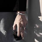 Hand with rings and bracelets holding a glass against a dark background