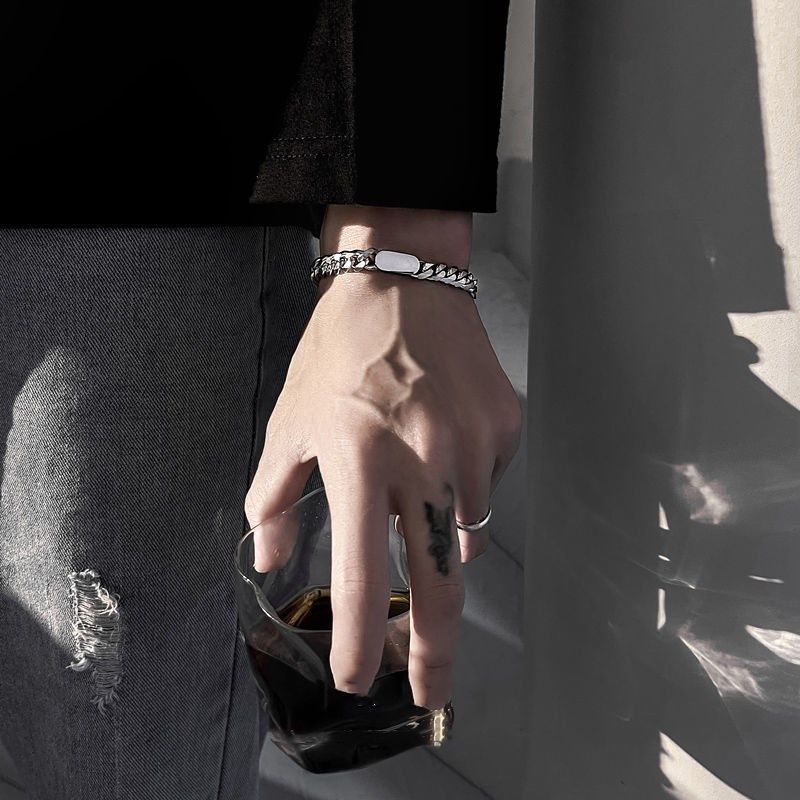Hand with rings and bracelets holding a glass against a dark background