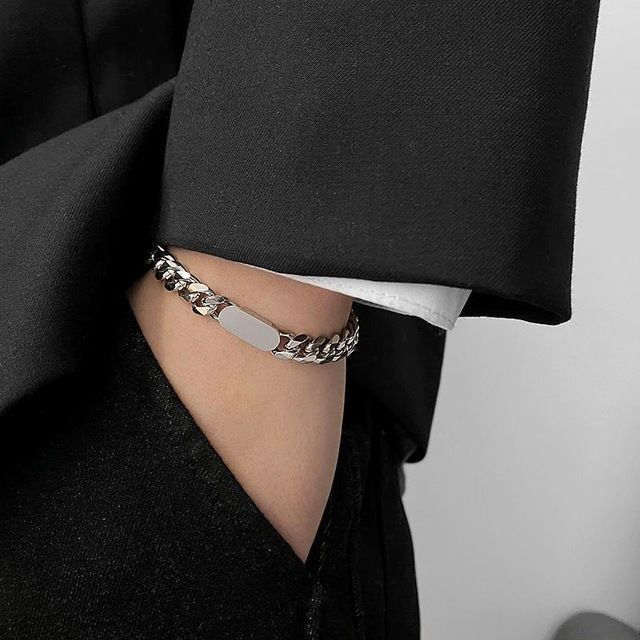 Person wearing a silver chain bracelet with a visible brand name on a plain background