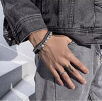 Person wearing bracelets and a ring on a hand with a tattoo, standing on white steps.