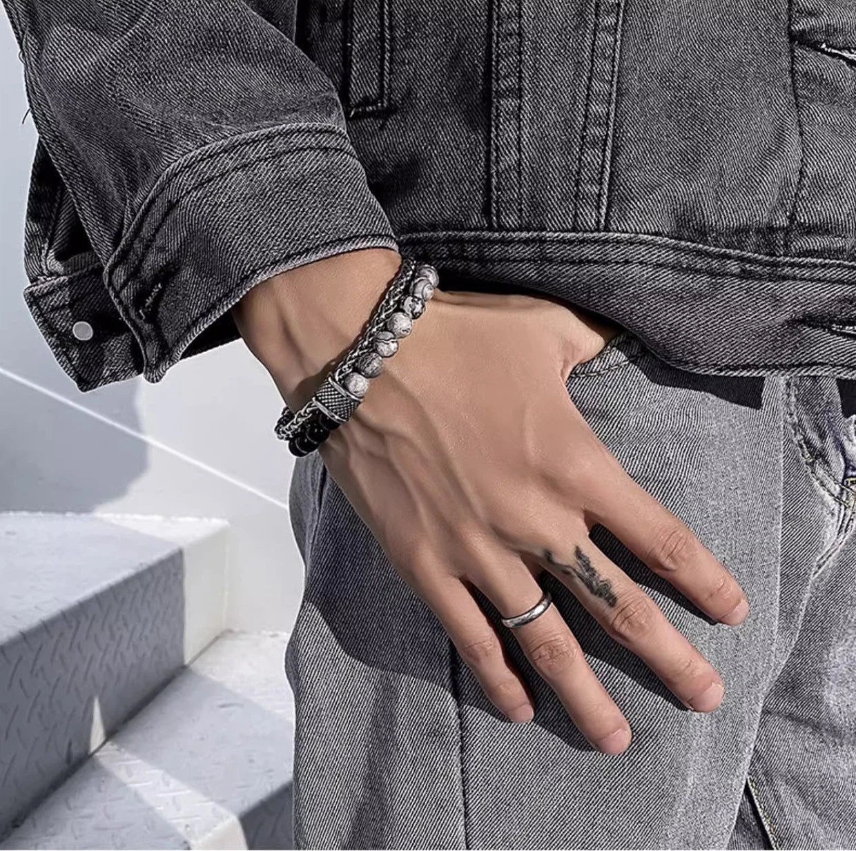 Person wearing bracelets and a ring on a hand with a tattoo, standing on white steps.