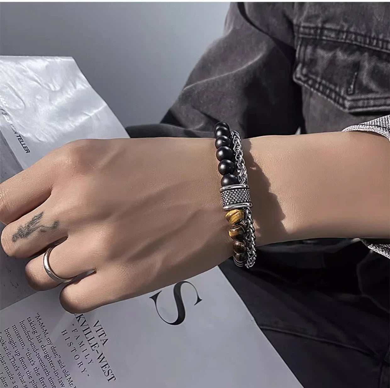 Hand wearing a bracelet with black beads and silver chain on a magazine background