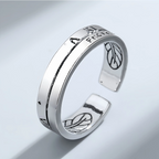 Silver open ring with engraved designs on a light gray background