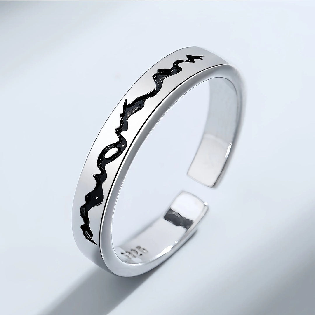 Silver ring with black engraved design on a light gray background