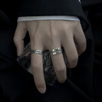 Close-up of a hand wearing two silver rings on a dark background