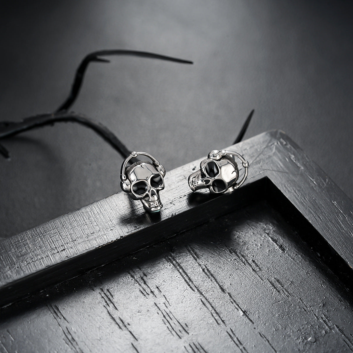 Skull-shaped earrings on a dark surface with a branch in the background
