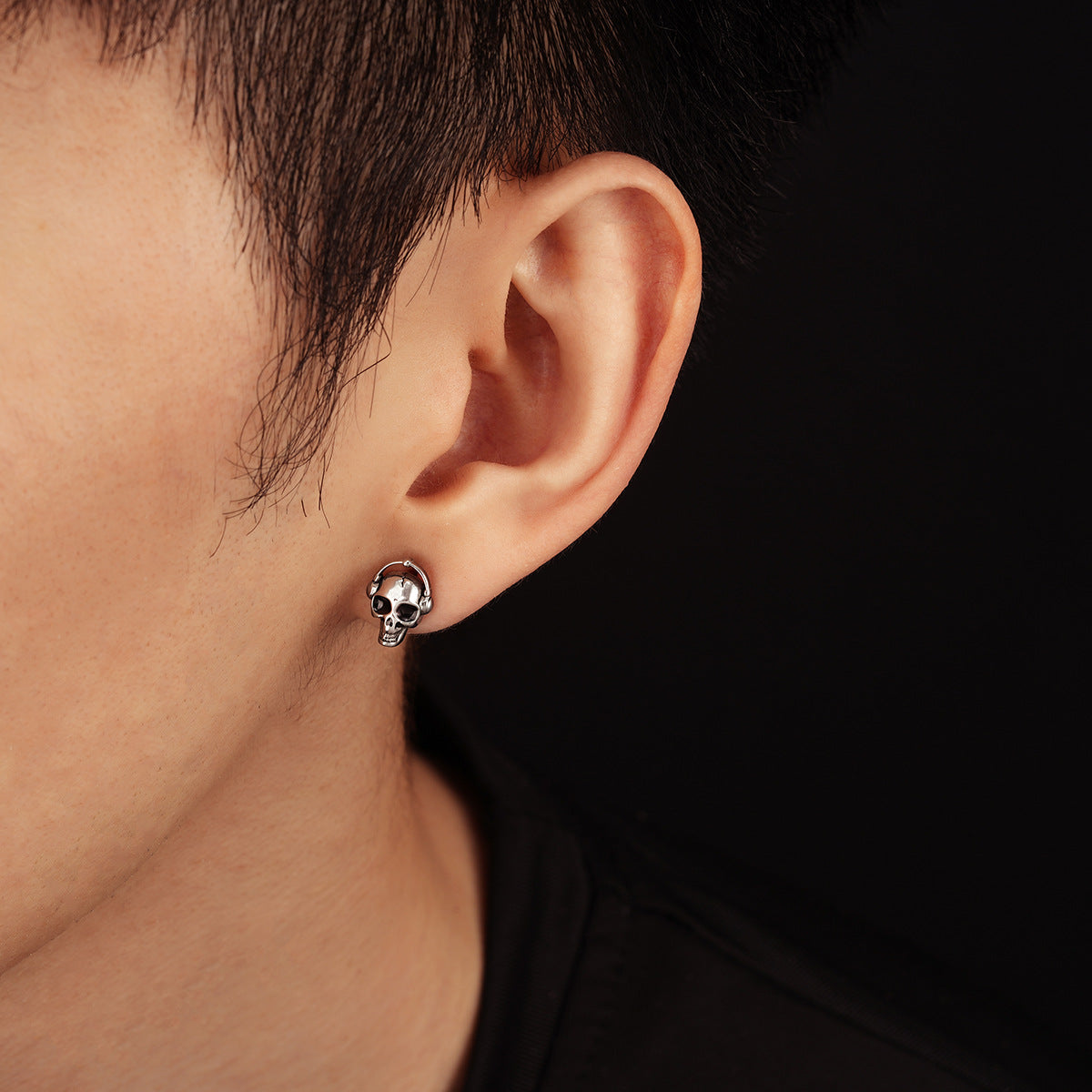 Close-up of an ear wearing a skull-shaped earring against a dark background