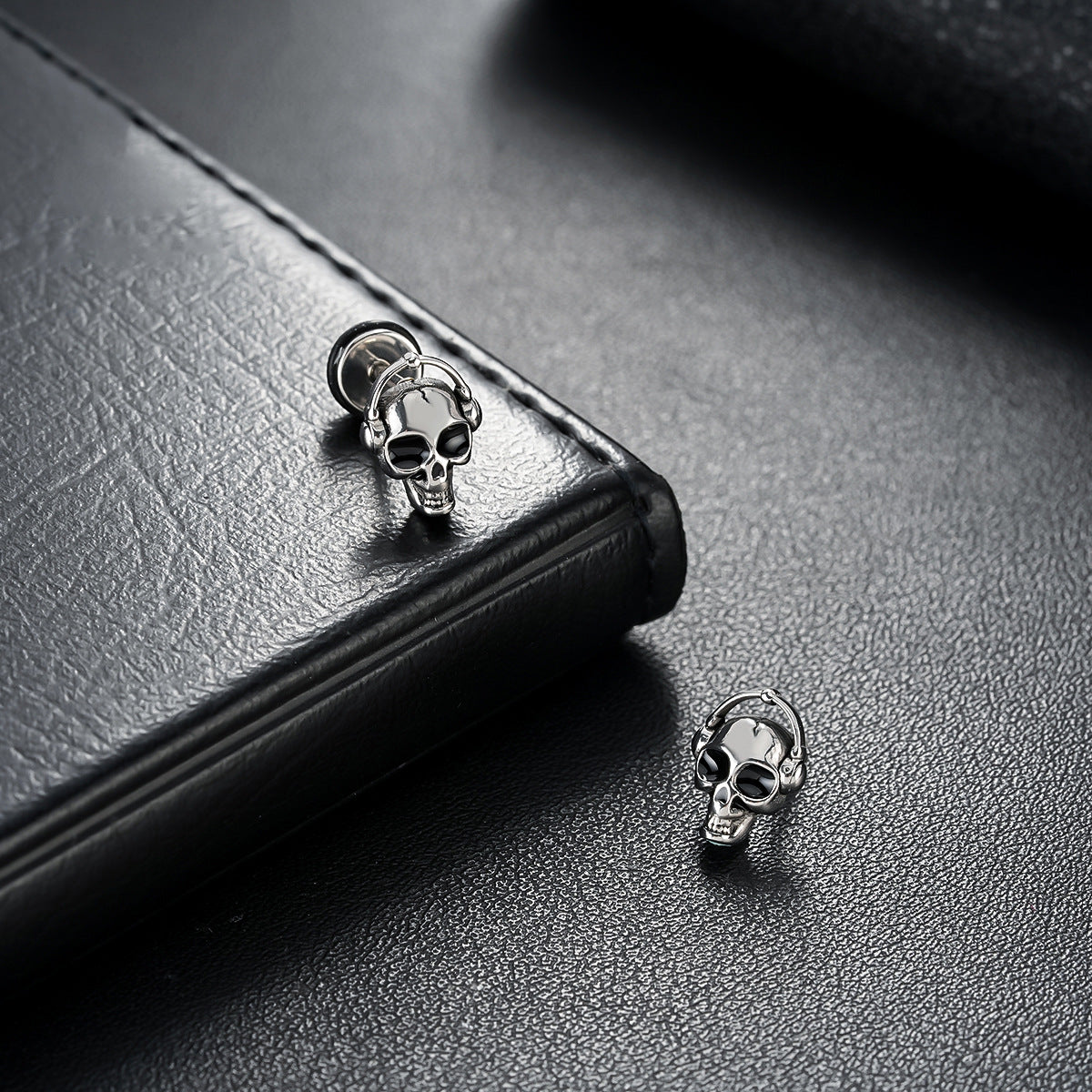 Skull-shaped earrings on a black leather surface