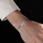 Silver bracelet with engraved text on a wrist against a black background