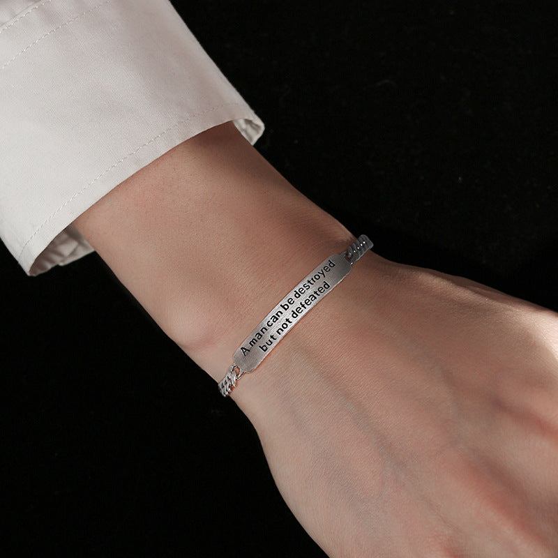 Silver bracelet with engraved text on a wrist against a black background