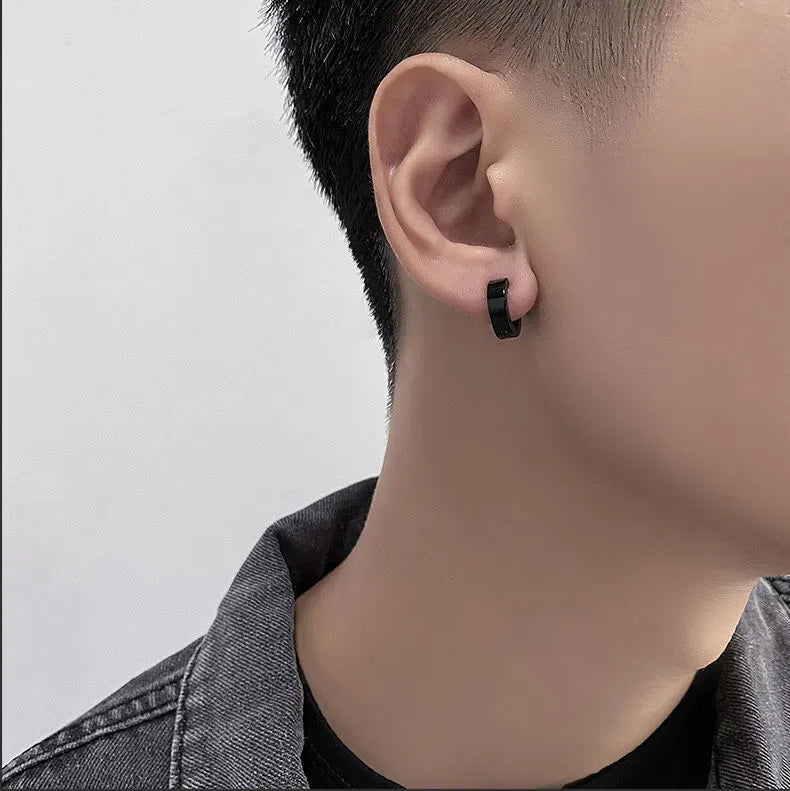 Close-up of a person wearing a black hoop earring on a plain background