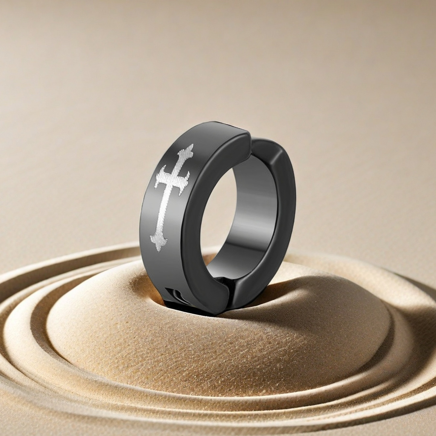 Black ring with a cross design on a beige sand-like surface
