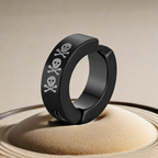 Black huggie hoop earrings with skull and crossbones design on a beige background
