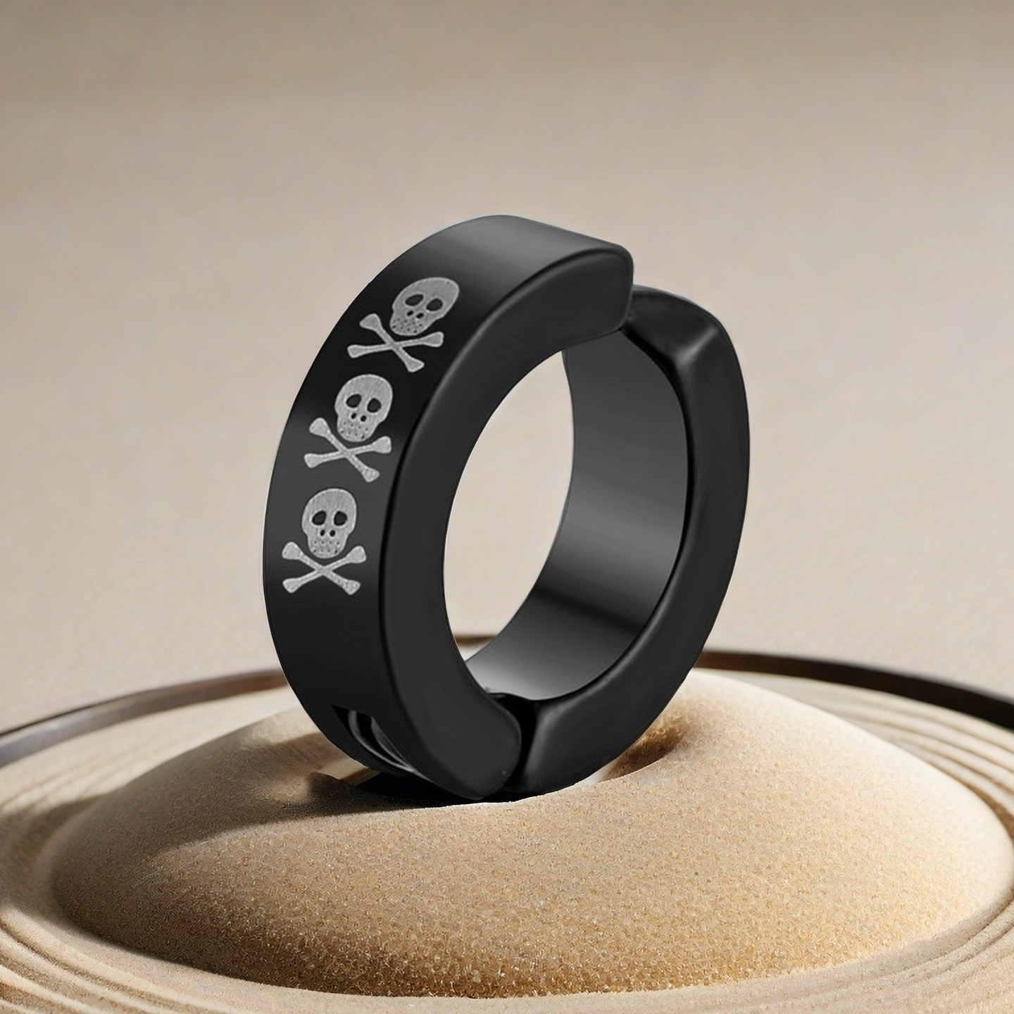Black huggie hoop earrings with skull and crossbones design on a beige background