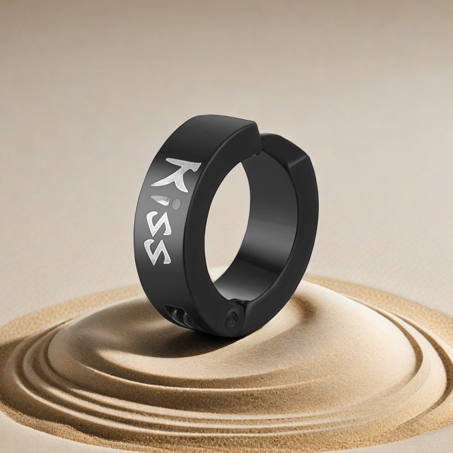 Black ring with 'KISS' engraving on a sand-like surface