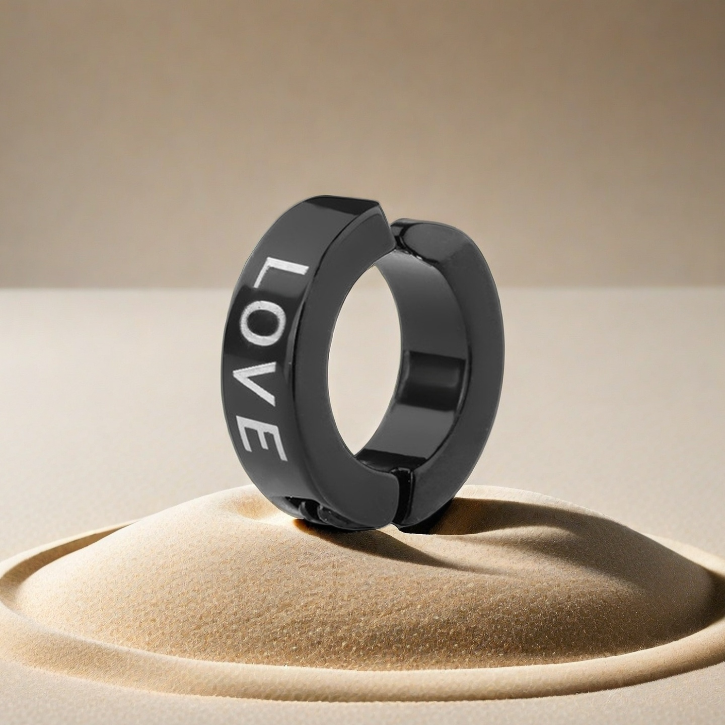 Black hoop earring with 'LOVE' engraving on a beige sand-like surface