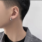 Close-up of a person wearing a silver hoop earring on a plain background