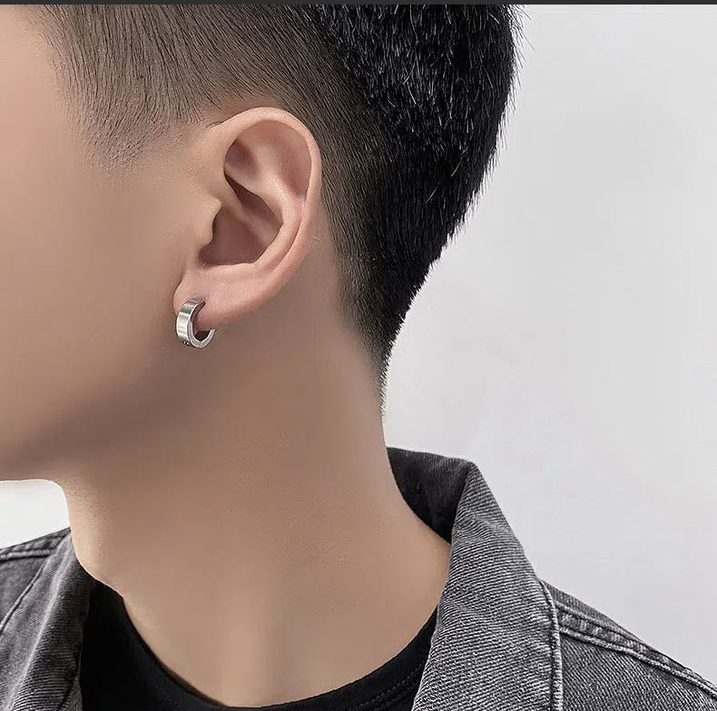 Close-up of a person wearing a silver hoop earring on a plain background