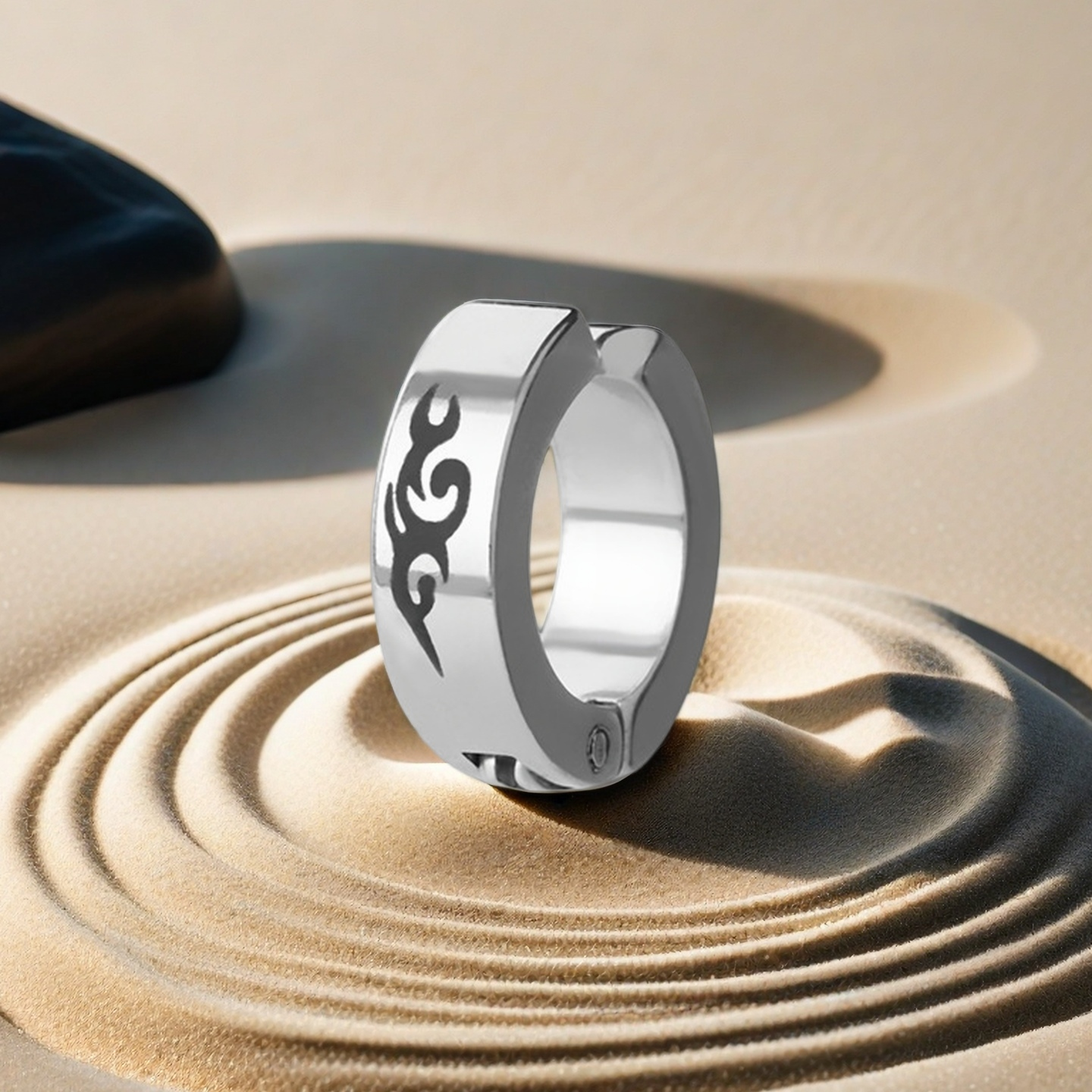 Silver ring with a black design on a sandy surface