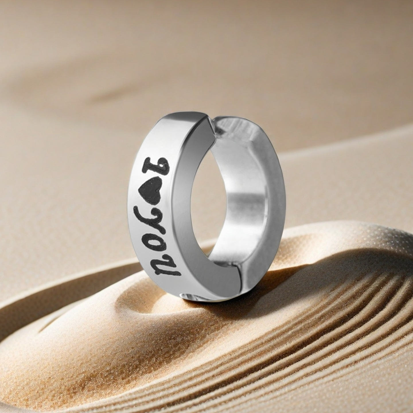 Silver hoop earring with 'I love you' engraving on a sandy background