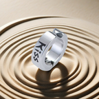 Silver ring with 'Kiss' engraving on a sand background
