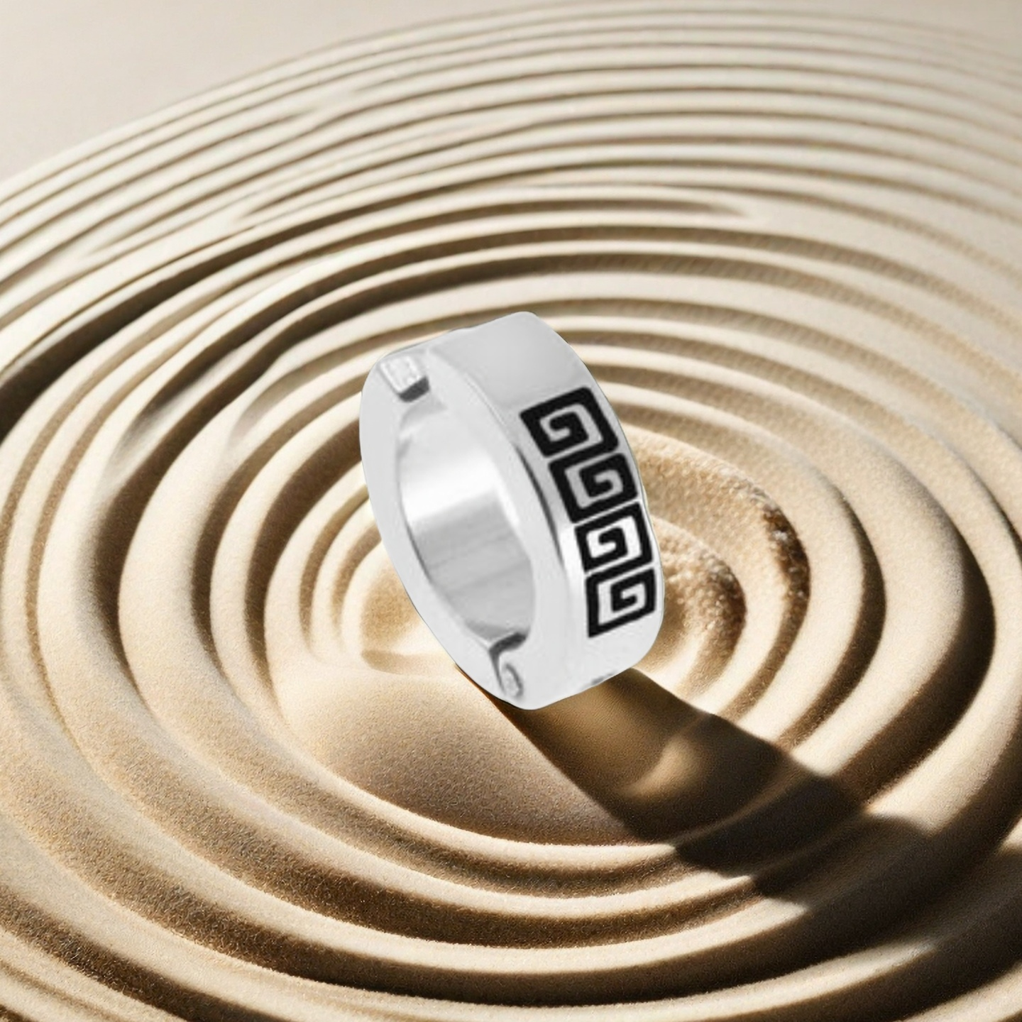 Silver ring with black geometric design on a sand background