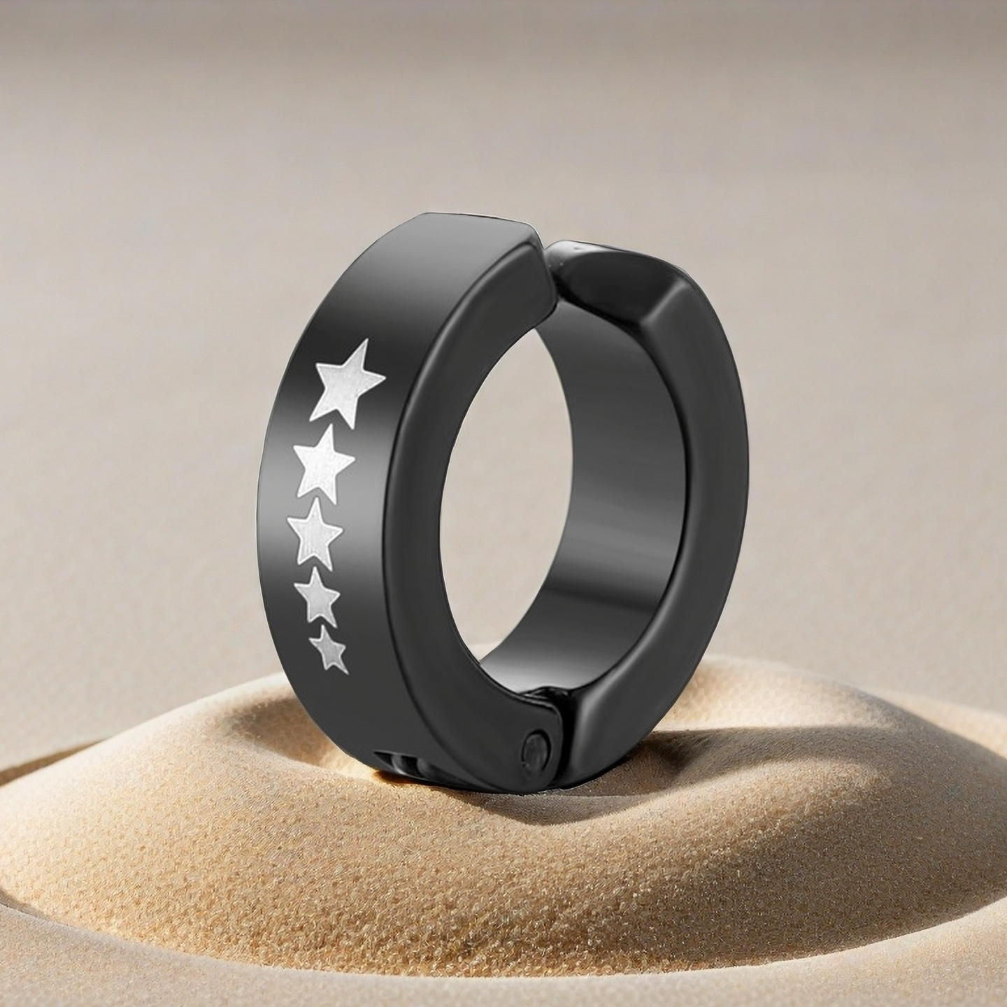 Black hoop earring with star designs on a beige sand-like surface