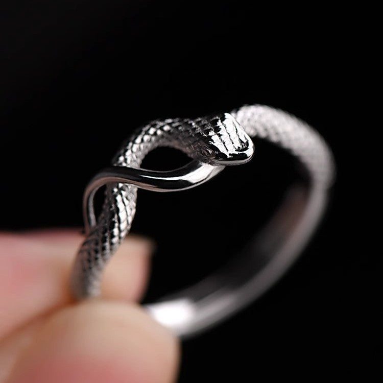 Silver snake-shaped bracelet held by a hand against a black background